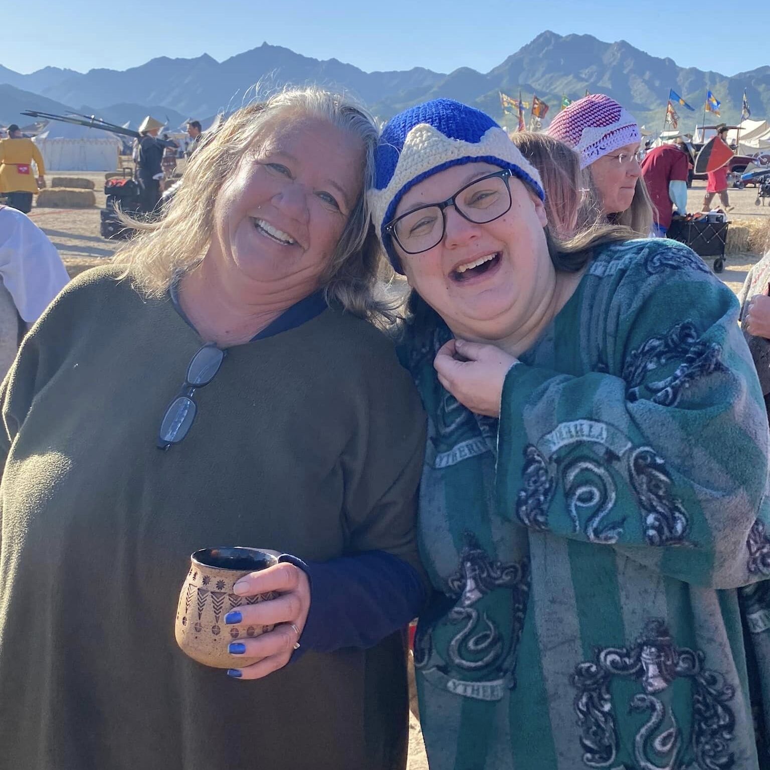 Two of the three Event Stewards for War of the Phoenix smiling and laughing candidly at a past War event. They're both wearing chilly weather robes and in the background a beautiful mountain range can be seen. You can contact these folks for questions on the event.