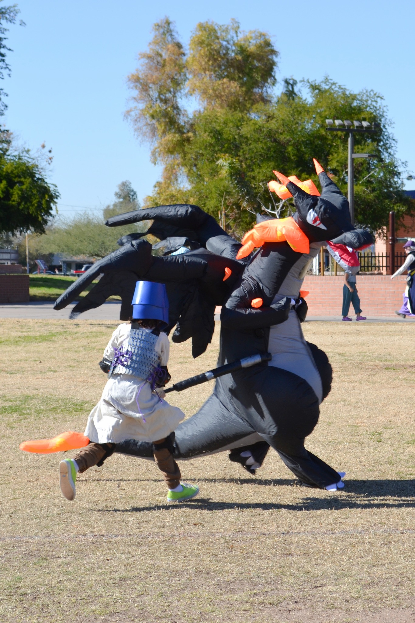 Young child in helm and boffer armour and garb defeating a beastly black (blow up) dragon in the soccer field.